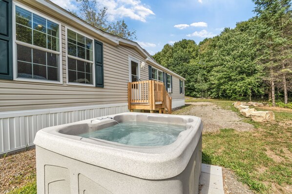 A house with a hot tub, wooden deck, and a stone pathway. - Welcoming 3-bedroom home with jacuzzi (Winterport)