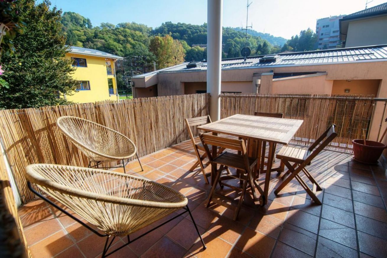 Eine Terrasse im Freien mit Tisch und Stühlen, einem Bambuszaun und Blick auf Gebäude und Bäume.