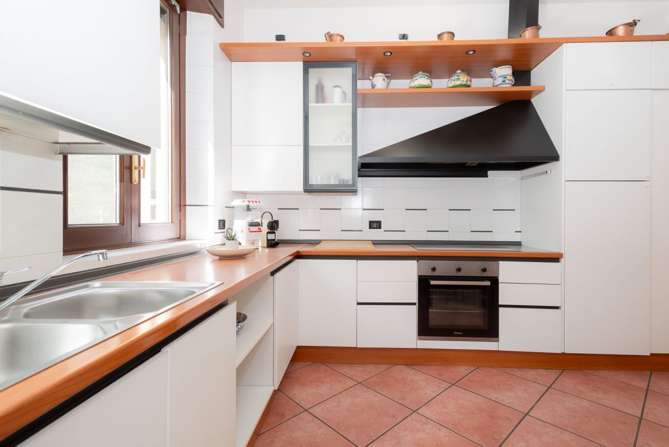 Een moderne keuken met witte kasten, een houten aanrecht, een inbouwoven en een zwarte afzuigkap.