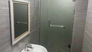 A bathroom with a glass shower enclosure, a white sink, and a mirror with a gold frame. - Infinity Luxury Apartment (Bwari)