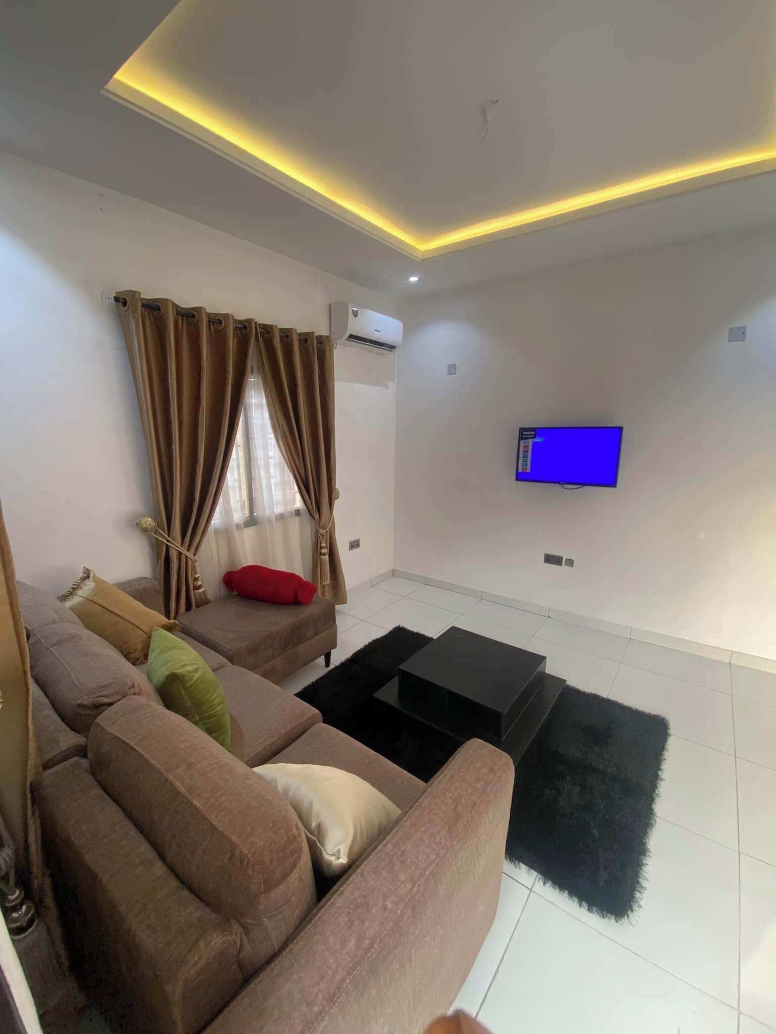 A modern living room with a sectional sofa, a flat-screen TV mounted on the wall, and a ceiling with recessed lighting.