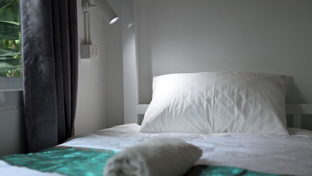 A hotel room with a bed, a window with curtains, and a wall-mounted light fixture. - Mays Hostel (Hua Hin)