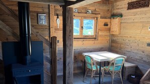 A rustic cabin interior with a wood stove, a dining table with chairs, and a window with a view of greenery. - Chalet “Mazot De La Pointe Percée” with Balcony (Combloux)