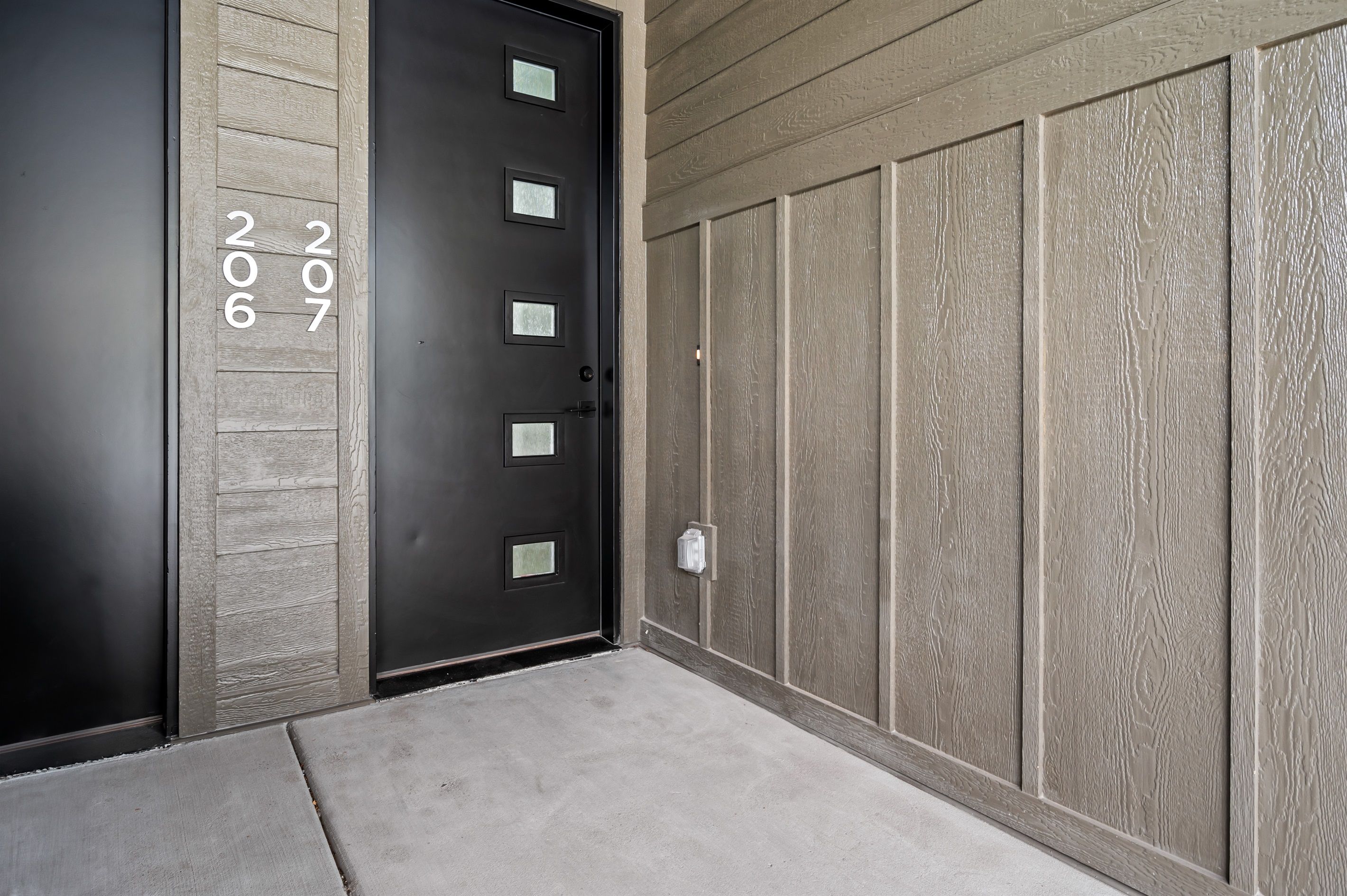 A modern building entrance with a black door marked with the numbers 206 and 207.