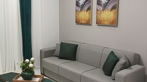 A modern living room with a grey sofa, green and patterned cushions, a wooden side table with a vase of flowers, and abstract paintings on the wall.