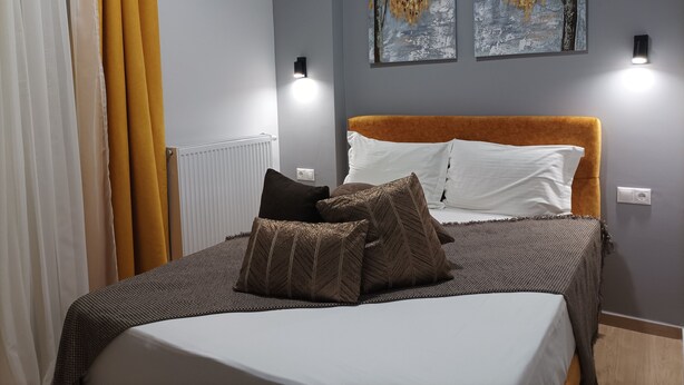 A bedroom with a bed, two wall-mounted lights, an air conditioner, and two paintings on the wall.