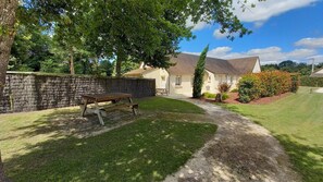 Une maison avec une allée pavée menant à la porte d’entrée, une table de pique-nique dans le jardin et un mur en pierre.