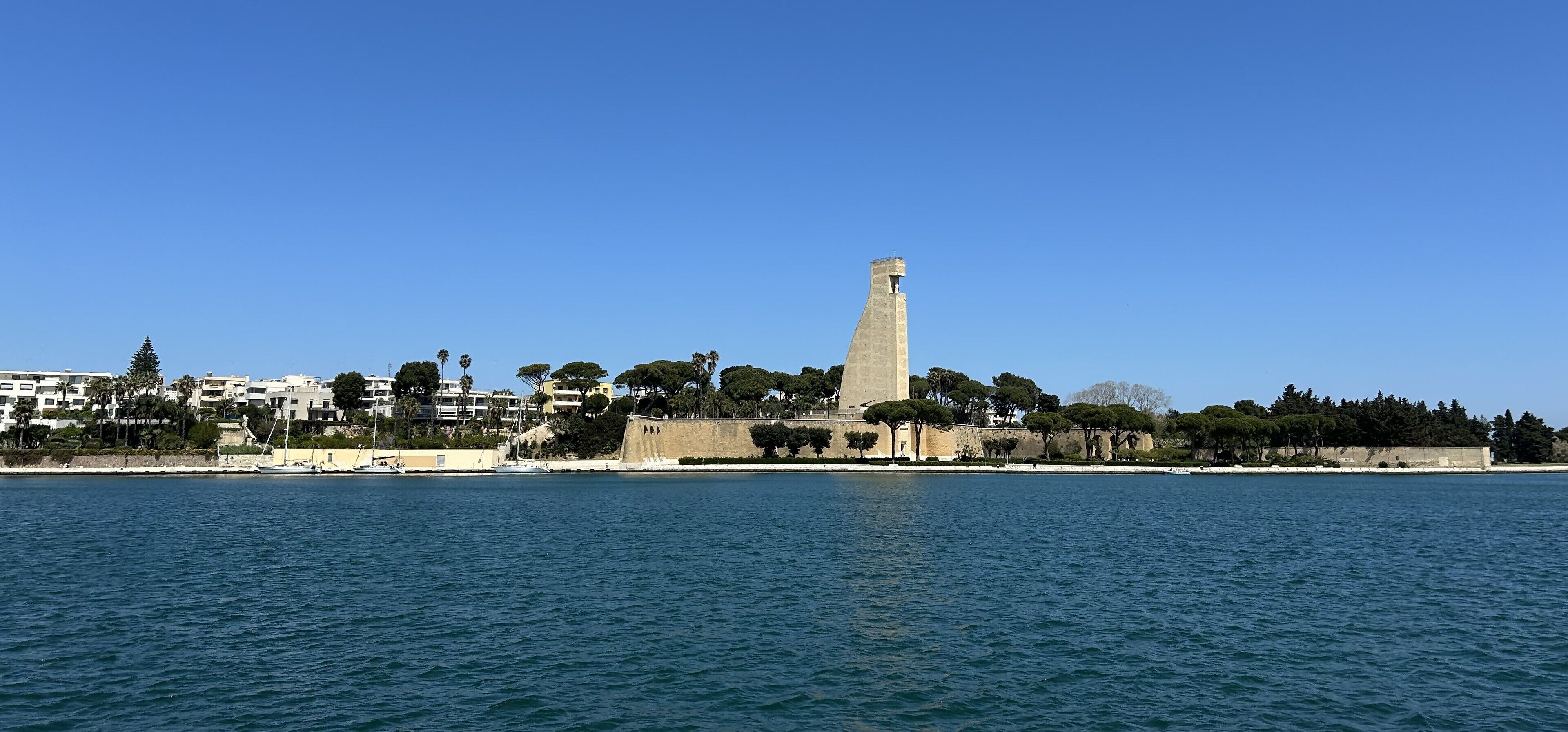 Een kuststadsgezicht met een opvallende toren, een promenade langs het water en woongebouwen.