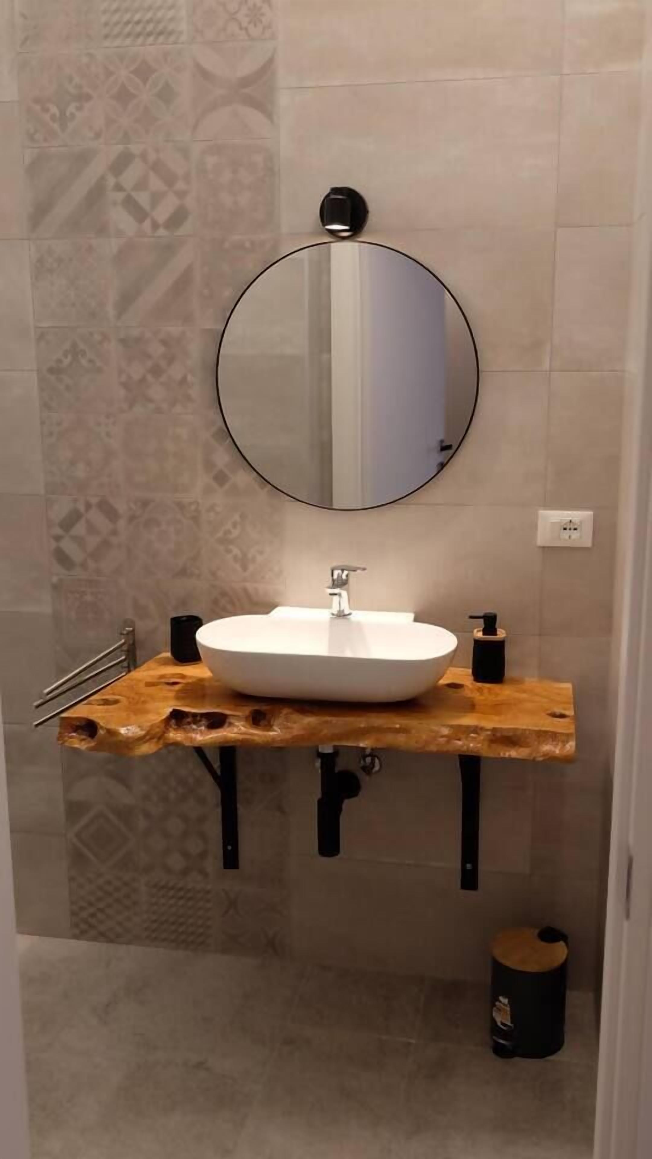 Une salle de bain avec un miroir rond, un lavabo blanc et un meuble-lavabo en bois.