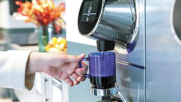 A hand holding a blue mug under a coffee machine.