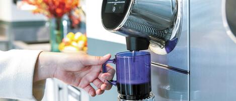 A hand holding a blue mug under a coffee machine.