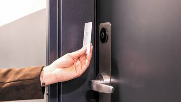 A hand holding a device near a door with a keypad and a lock.
