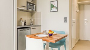 Cocina compacta con microondas, pileta y lavavajillas. Cuenta con una mesa de comedor, sillas y un bol de frutas.