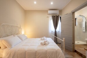 Quarto com cama, janela com cortinas, ar condicionado e porta de vidro para o chuveiro.