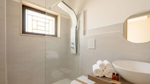 Une salle de bain moderne dotée d’une douche à parois de verre, de toilettes, d’un lavabo avec un grand bac et d’une fenêtre laissant entrer la lumière naturelle.