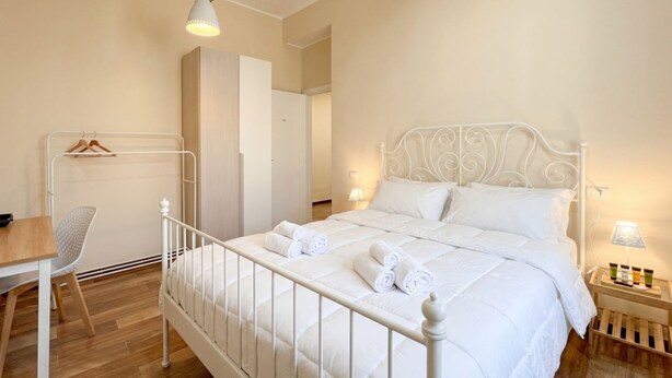 Une chambre avec un lit en métal blanc, un bureau en bois, une chaise et un portant à vêtements.