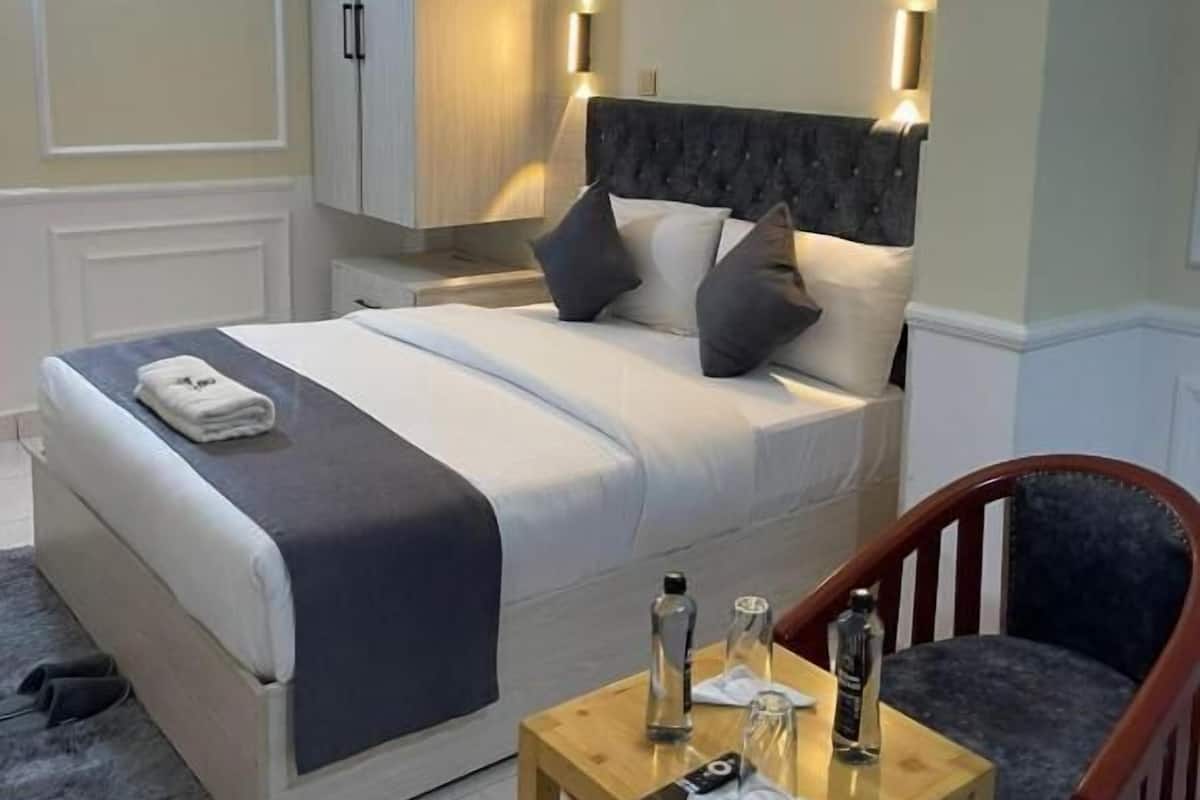 Un dormitorio ordenado con cama, mesitas de noche, una silla y un espejo.