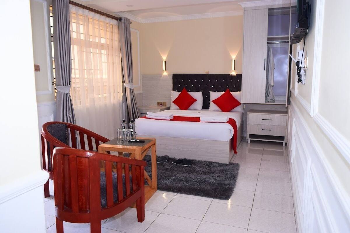 Habitación de hotel con cama, mesita de noche, silla y televisor montado en la pared.