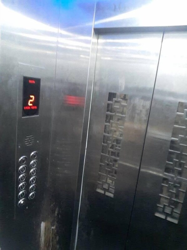 An elevator interior with a digital display showing the number 2, a keypad, and a metallic door with a handle. - Hotel Annapurna (Khambhaliya)