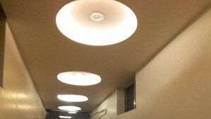 Un couloir avec des spots encastrés au plafond, une porte au fond et une petite fenêtre sur le mur de droite.