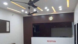 Un espace d’accueil comprenant un comptoir de réception portant l’inscription « RÉCEPTION », un ventilateur de plafond et deux canapés marron.