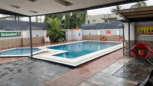 Área de piscina ao ar livre com sinal da Heineken, cadeira de salva-vidas e placa de segurança.