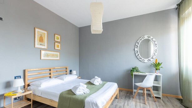 Un dormitorio ordenado con cama, mesita de noche, silla y escritorio con espejo.