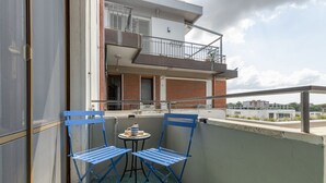 Un balcón con dos sillas plegables azules y una pequeña mesa, con vista a un edificio que tiene también un balcón y vistas a otros edificios.