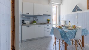 Una cocina compacta con armarios blancos, una mesa de comedor con mantel azul y una ventana con vistas.