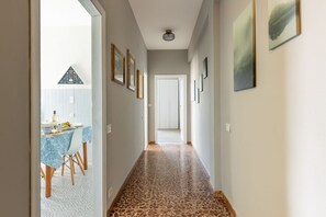 Un pasillo con suelo estampado, cuadros enmarcados en las paredes y una mesa con sillas al fondo.