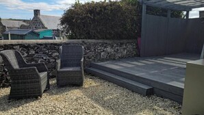 Un patio con dos sillas de mimbre, una terraza de madera y un muro de piedra.