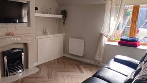 Una sala de estar con chimenea, televisor montado en la pared, un sofá y una ventana con cortinas.