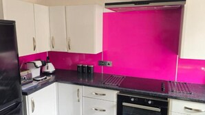 Una cocina con armarios blancos, un refrigerador negro, salpicadero rosa y una cafetera.