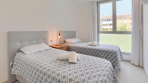 Ett hotellrum med två sängar, ett nattduksbord, en lampa och ett stort fönster med utsikt över byggnader.