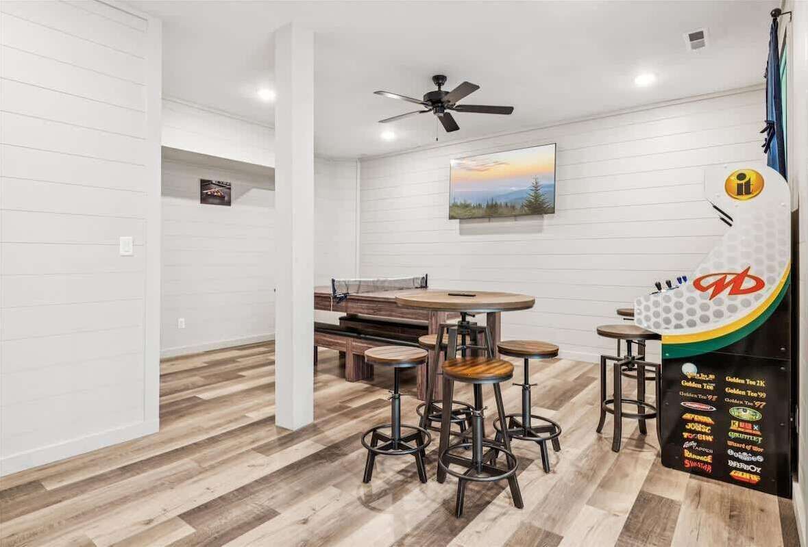 Une cuisine moderne avec des murs en bois peints en blanc, un plancher en bois, un ventilateur de plafond et un coin bar avec des tabourets et un tableau affichant le menu.