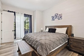 Un dormitorio con una cama de madera, una banca, una mesita de noche y vistas al exterior a través de una ventana con cortinas.