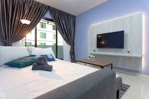 A modern hotel room with a large bed, a flat-screen TV mounted on the wall, a small table with a vase of flowers, and a window with curtains. - Cozy JB Suasana 15 Suite, City Views (Johor Bahru)