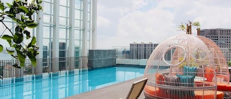 Un área de piscina en la azotea con vistas despejadas del horizonte urbano, un amplio ventanal y una estructura esférica de asientos singular.