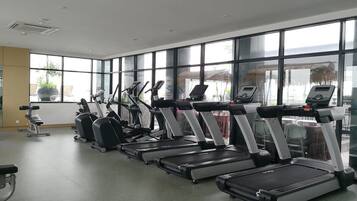 Een sportschool met loopbanden en hometrainers, grote ramen en een groene vloer.