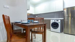 A modern kitchen with white cabinets, a stainless steel refrigerator, a washing machine, and a dining table with chairs. - Cozy JB Suasana 15 Suite, City Views (Johor Bahru)