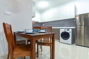 Une cuisine moderne avec des meubles blancs, un réfrigérateur en acier inoxydable, un lave-linge et une table à manger avec des chaises.