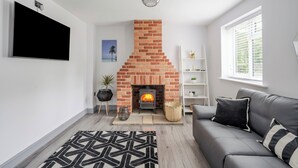 Ein Wohnzimmer mit Kamin aus Backstein, einer grauen Couch und einem gemusterten Teppich.