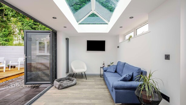 Ein modernes Wohnzimmer mit Dachfenster, einem blauen Sofa, einem weißen Sessel und einem Hundebett.