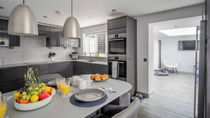 Eine moderne Küche mit grauen Schränken, einer zentralen Kochinsel mit Obst und Getränken sowie Blick auf einen Balkon.