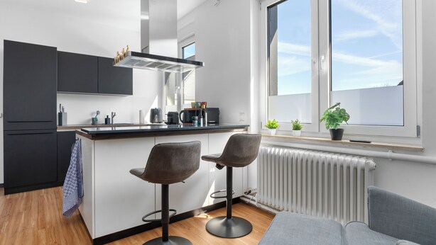 A modern kitchen with two bar stools, a large window, and a view of the sky.