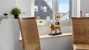 A room with two wicker chairs, a small golden lion statue, a potted plant, and a view of a house through a window.