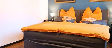 A bedroom with a bed, two wall-mounted paintings, a nightstand, and a blue rug.