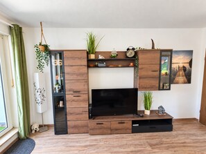 A modern living room with a flat-screen TV, wooden entertainment unit, and a window with curtains.