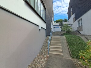 Un sendero estrecho que conduce a un edificio de diseño moderno, con una escalera de concreto y una barandilla de metal.
