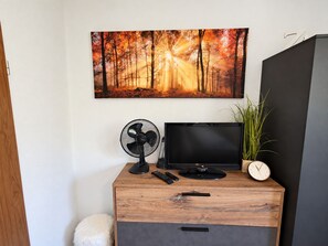 Un escritorio de madera con un televisor de pantalla plana, un ventilador, un reloj y un control remoto.
